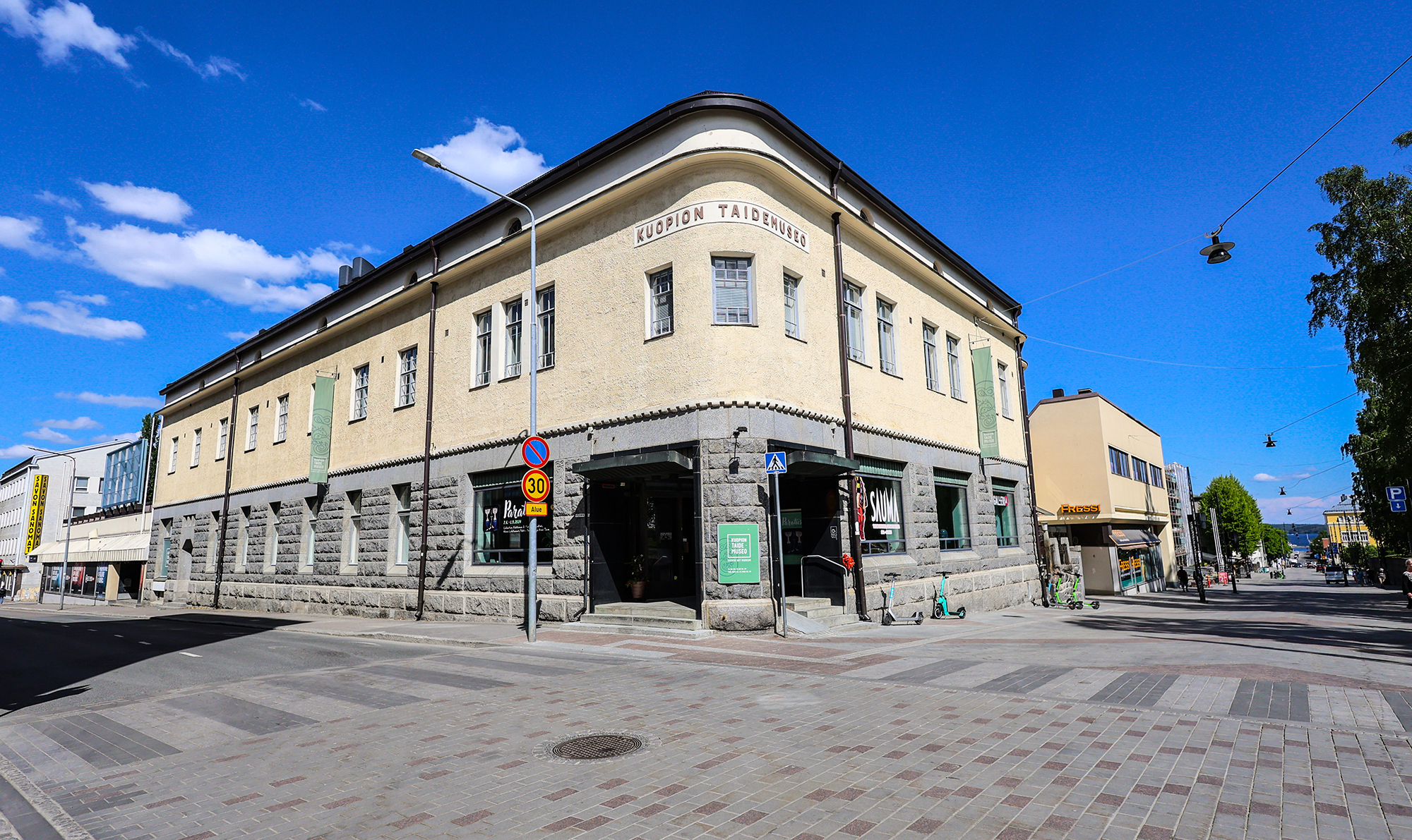 Taidemuseorakennus kesäisessä ympäristössä. Kuvan etualalla katulauetta.