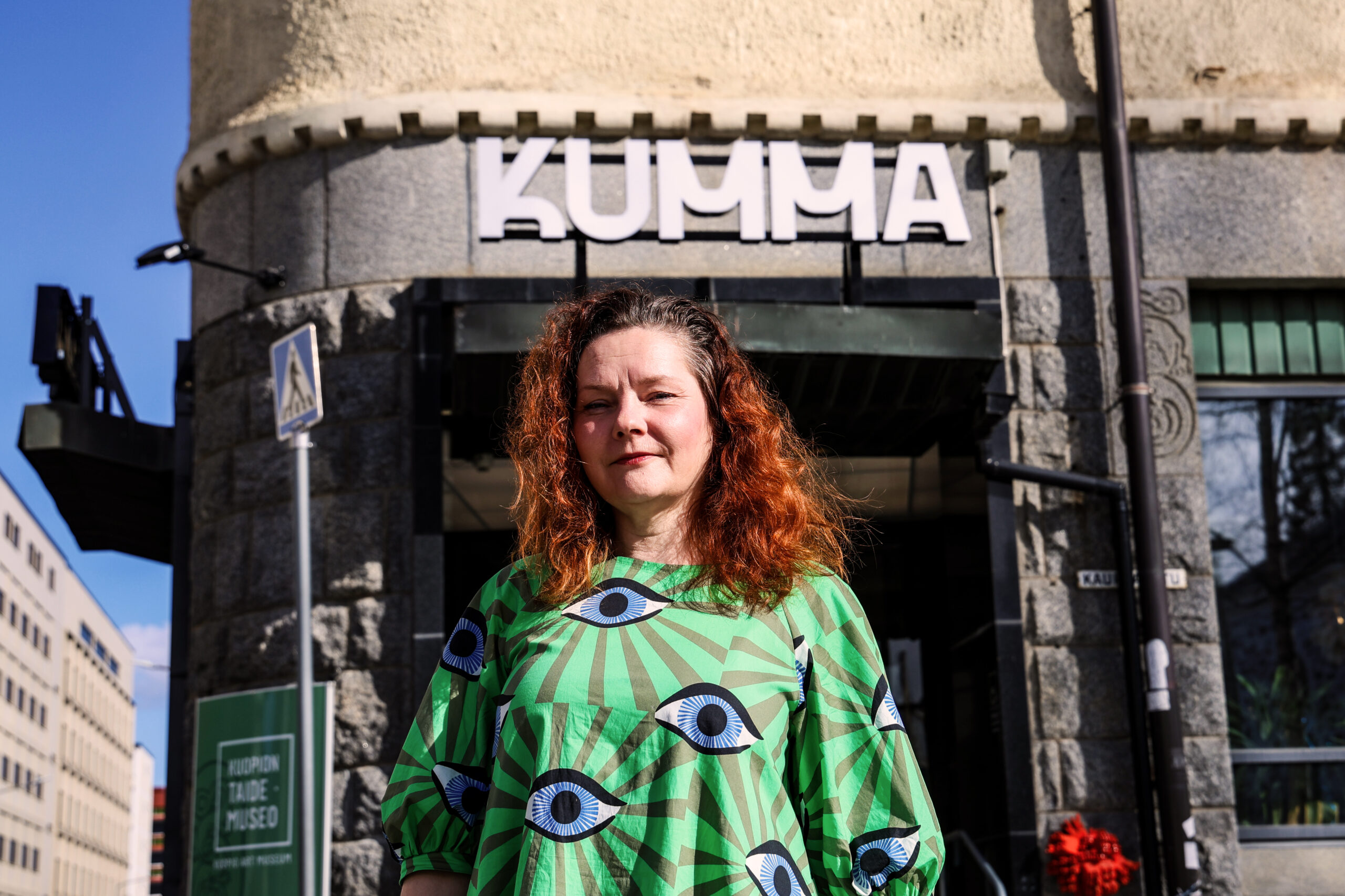Henkilö seisoo rakennuksen edessä, jonka kyltissä lukee KUMMA.